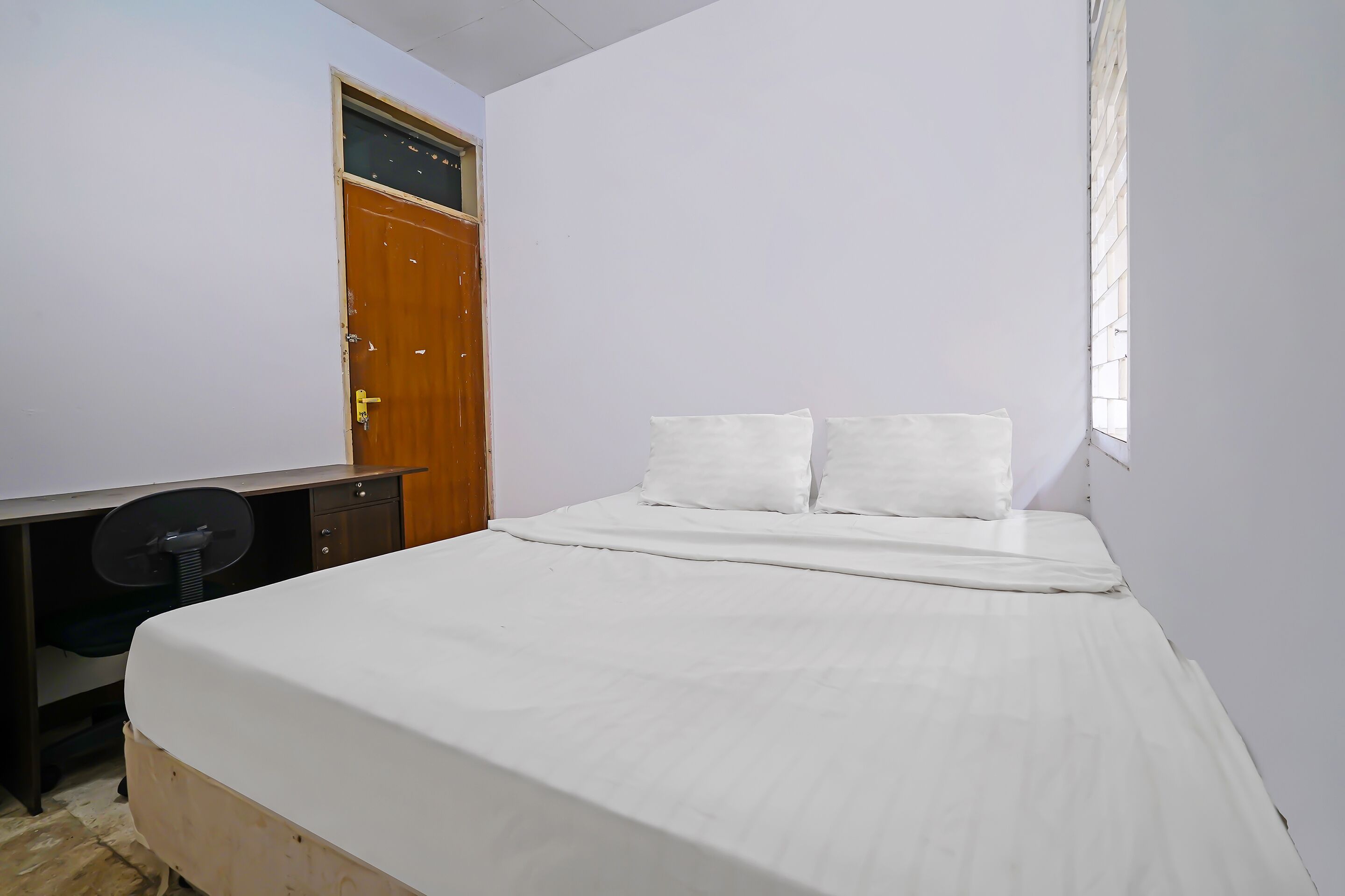 A bedroom with a single bed, a wooden desk with a chair, and a door.