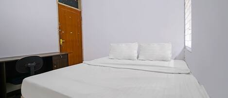 A bedroom with a single bed, a wooden desk with a chair, and a door.