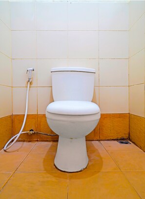 A standard toilet is situated in a corner of the bathroom, surrounded by beige and orange tiles.