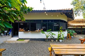 Relax in a serene outdoor seating area with a thatched roof, wooden tables, and lush greenery.