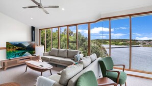 Amplia sala de estar con un televisor grande, asientos cómodos y una vista panorámica de un lago y vegetación.