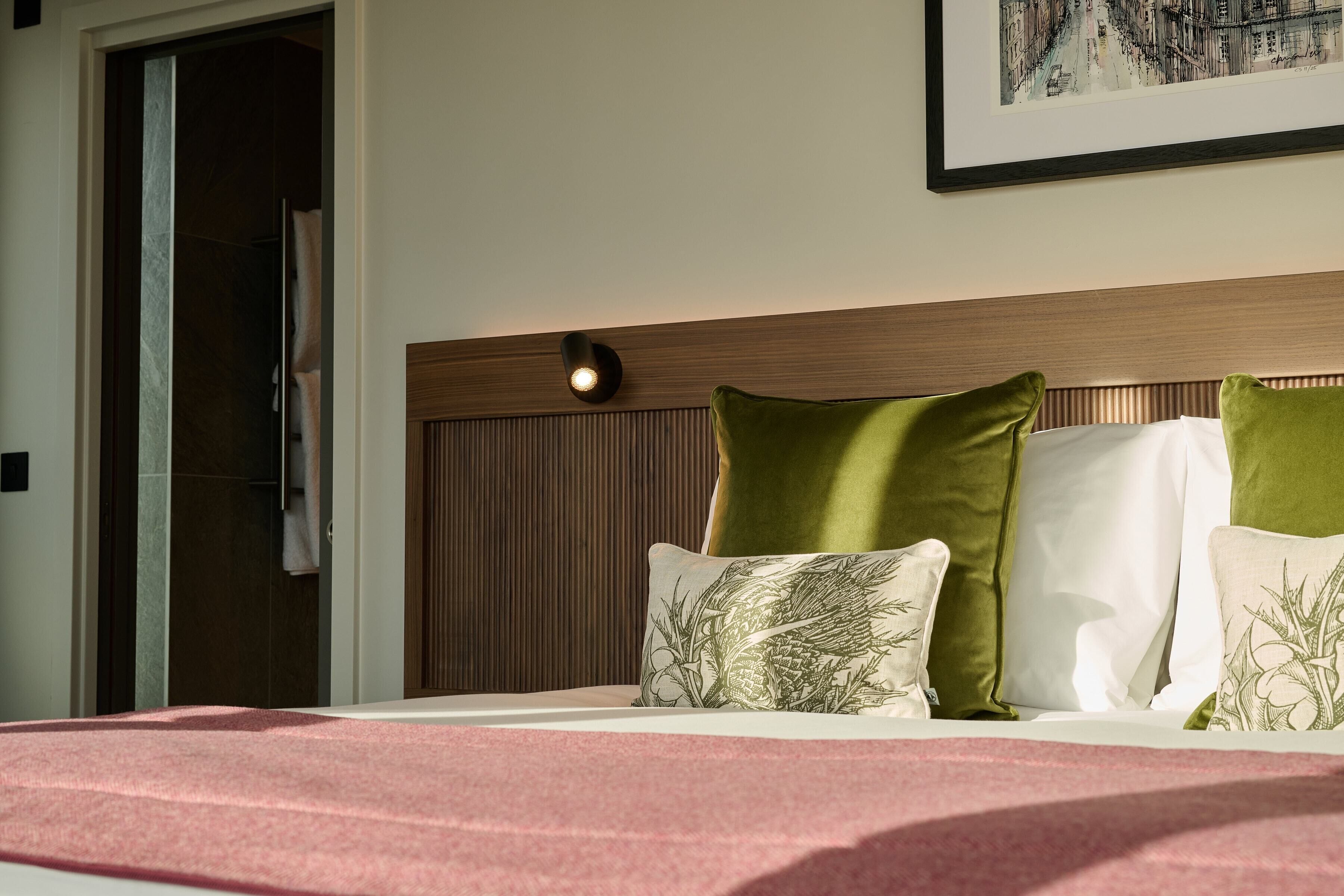 A hotel room with a bed, a headboard with a light fixture, and a framed picture on the wall.