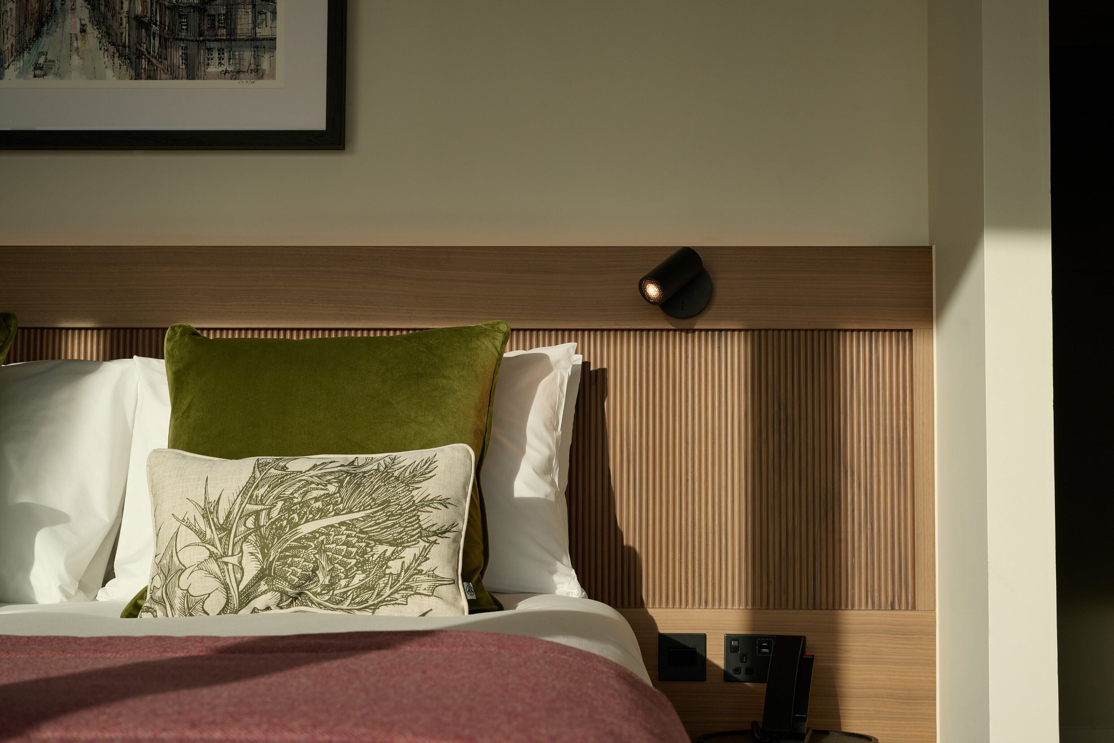 Un lit bien fait, avec un oreiller vert et blanc, une tête de lit en bois et une table de chevet surmontée d’une lampe.