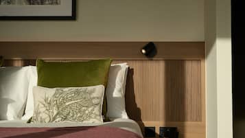 Un lit bien fait, avec un oreiller vert et blanc, une tête de lit en bois et une table de chevet surmontée d’une lampe.