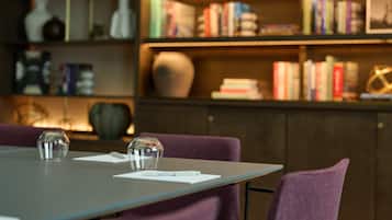 Een moderne eetruimte met een tafel voor twee personen, omringd door paarse stoelen. Achtergrond toont een boekenkast vol boeken en decoratieve objecten.
