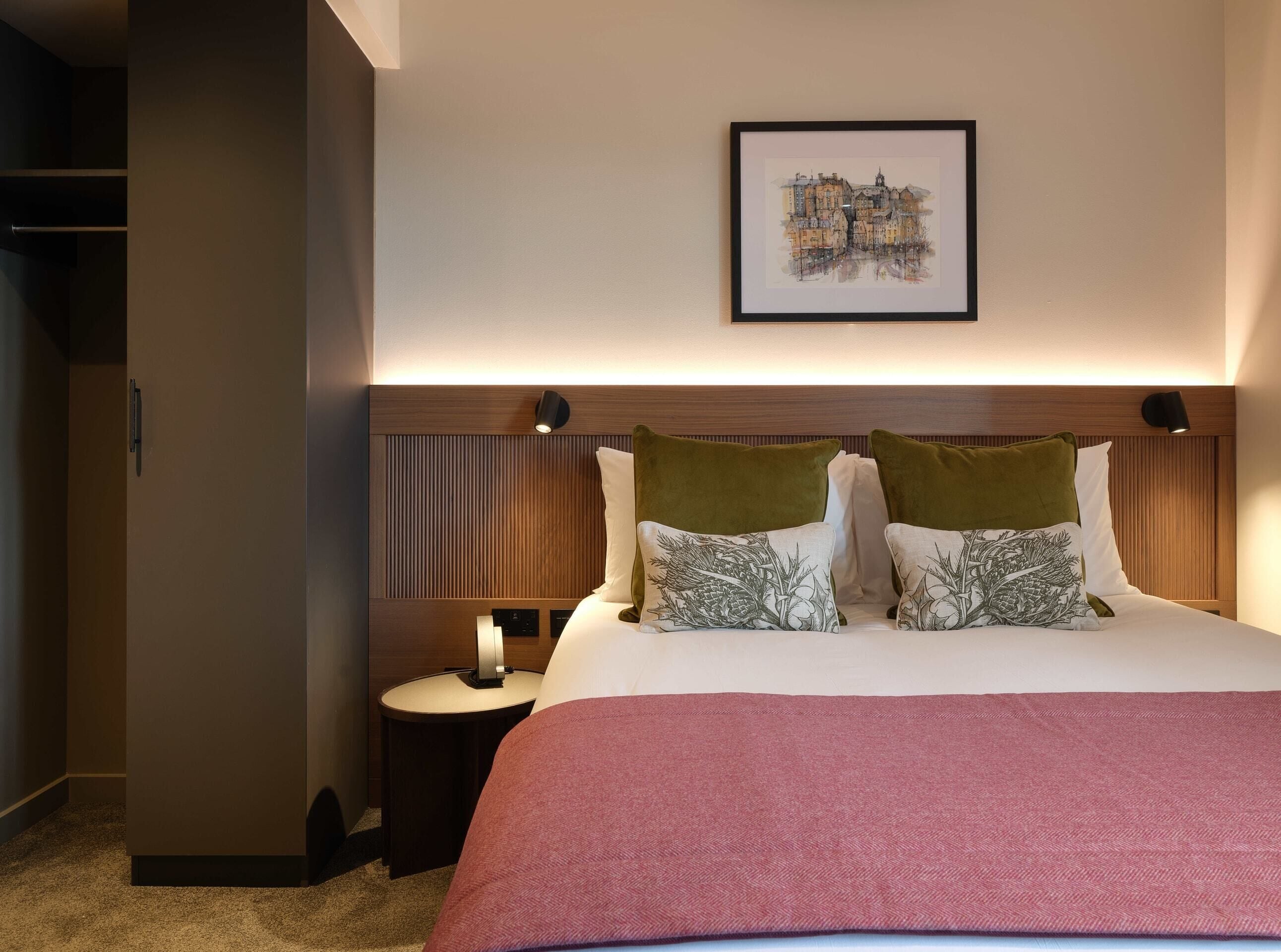 Una habitación de hotel con cama, mesita de noche, un cuadro enmarcado en la pared y un armario.