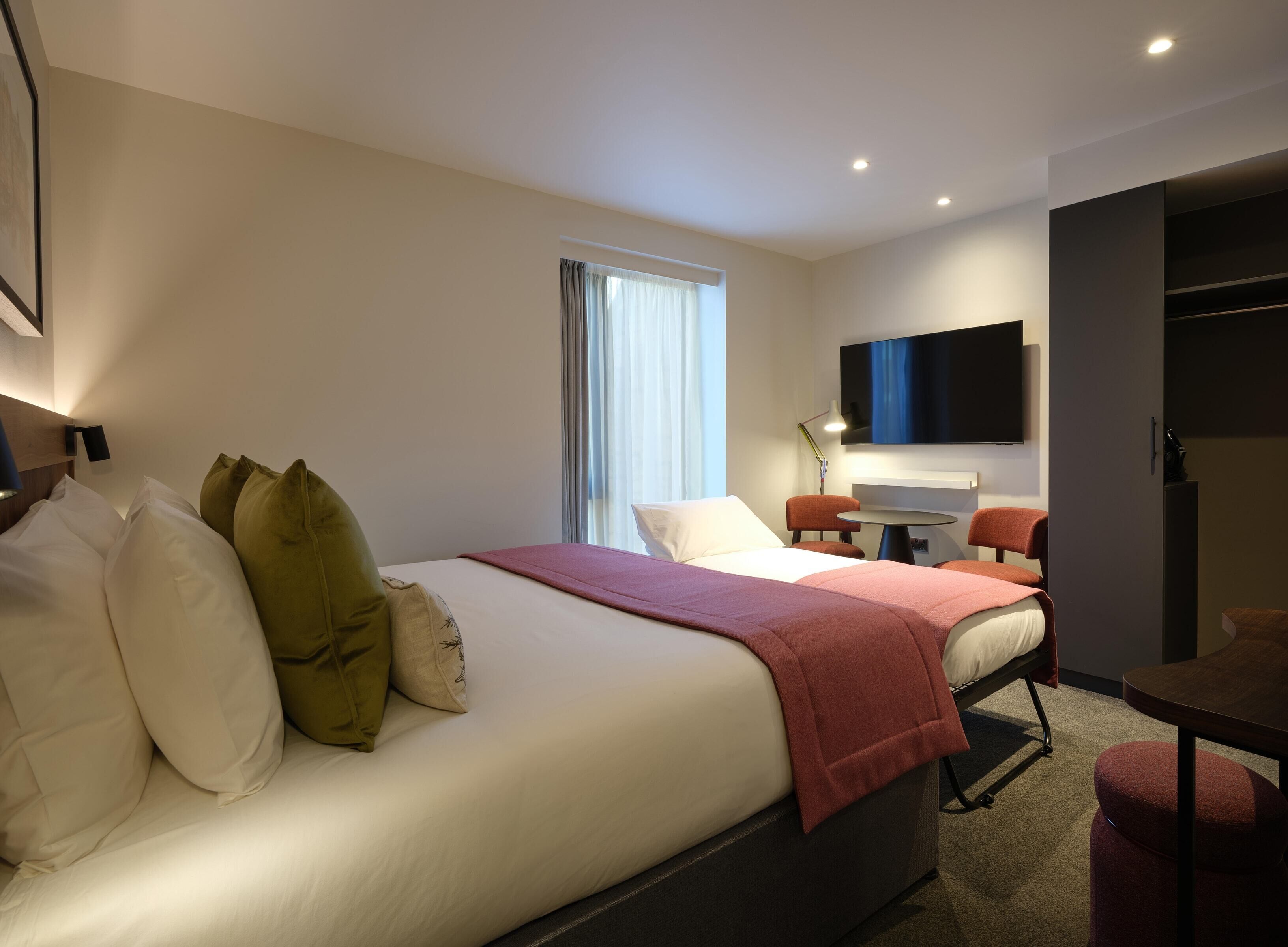 A modern hotel room with a large bed, a desk, and a TV.