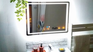 A bathroom with a white sink, a mirror with a light, and a plant.