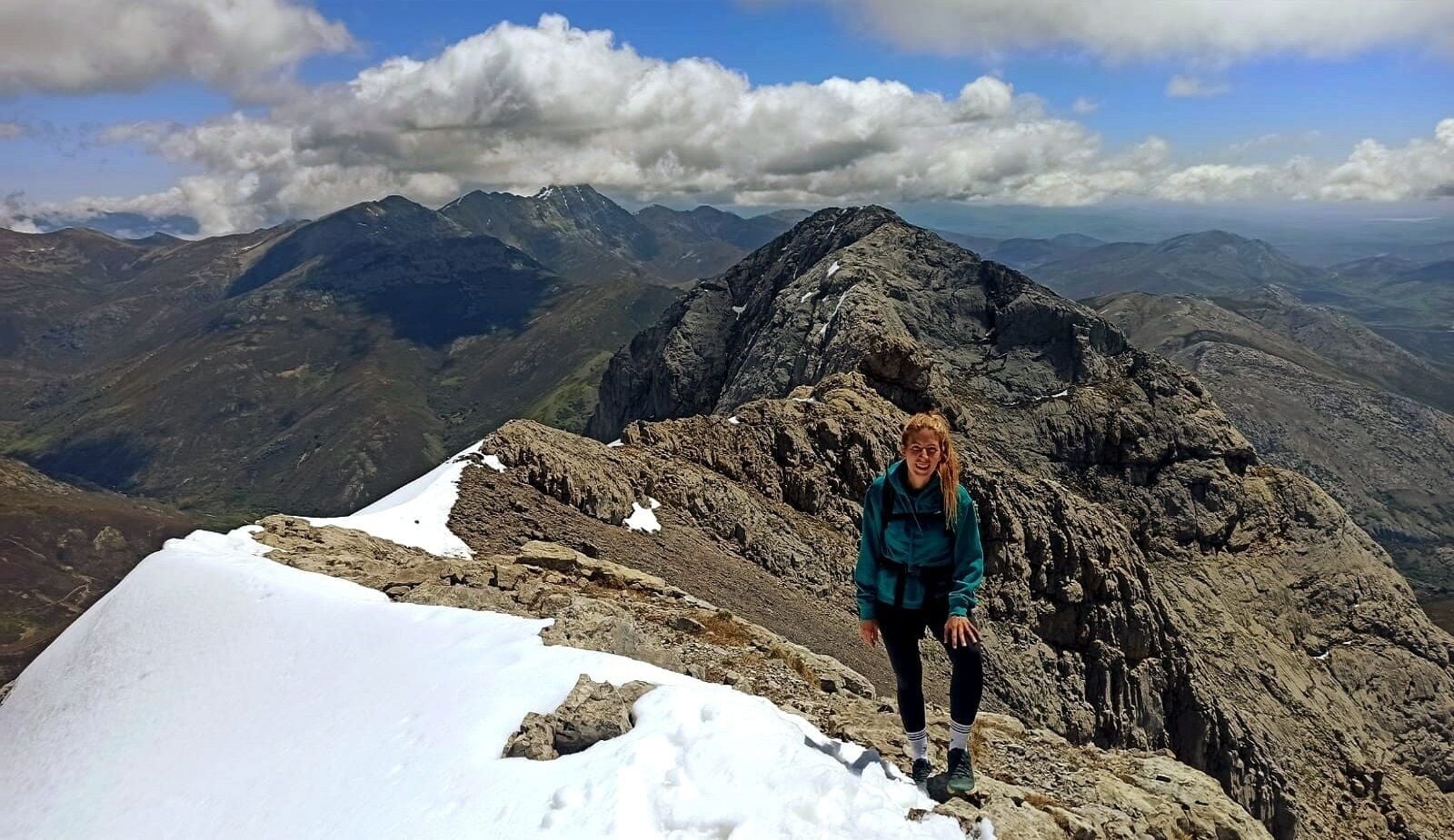 Una persona de pie en la cima de una montaña nevada, con vistas a montañas escarpadas al fondo.