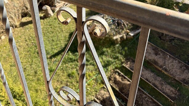 A scenic view from a balcony with a metal railing, overlooking a lake, forested hills, and a distant town.