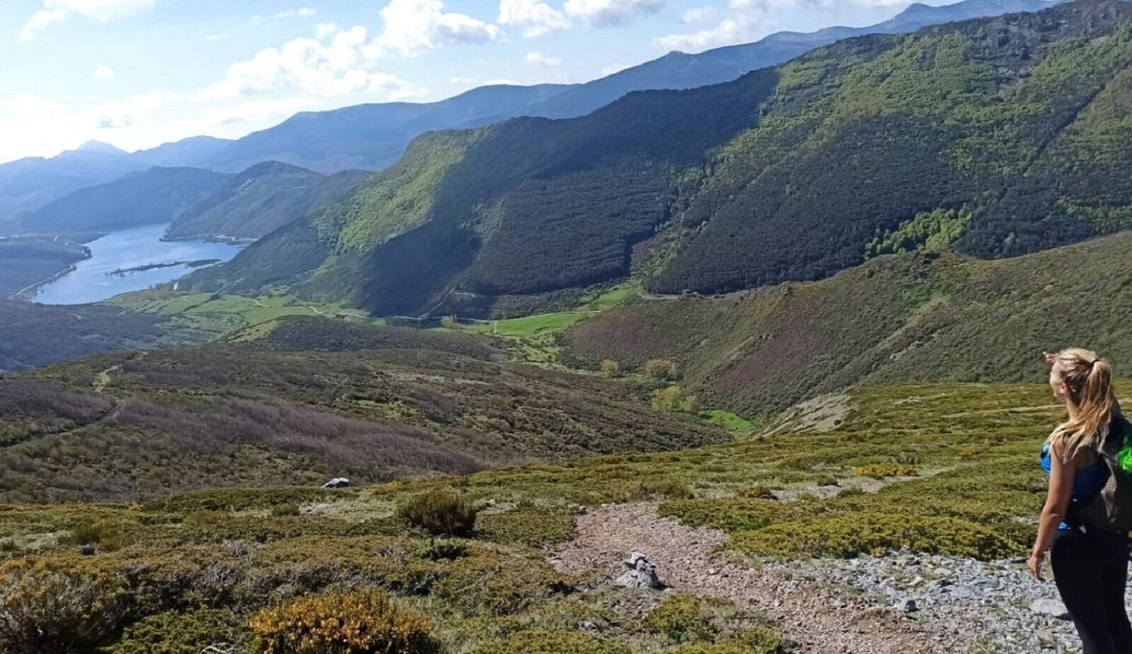 Ein Wanderer auf einem Bergpfad mit Blick auf einen See und ferne Berge.