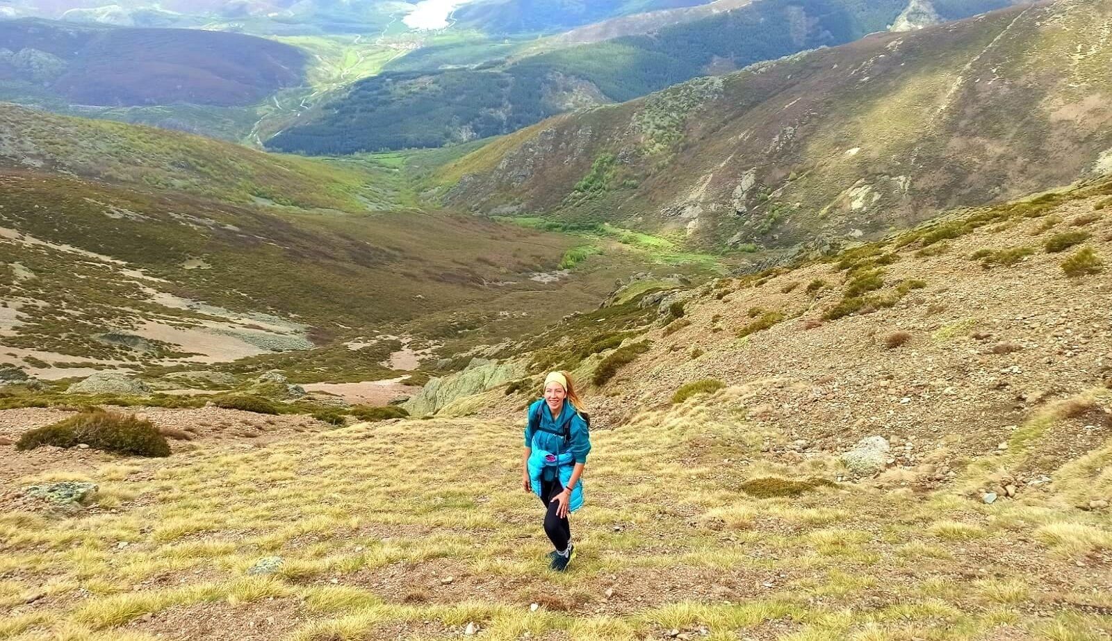 A person hiking on a grassy hillside with a valley in the background.
