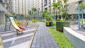 A playground with a slide and swings, surrounded by greenery and a paved path. - OYO Life 92718 Apartement Gateway Cicadas (Bandung)