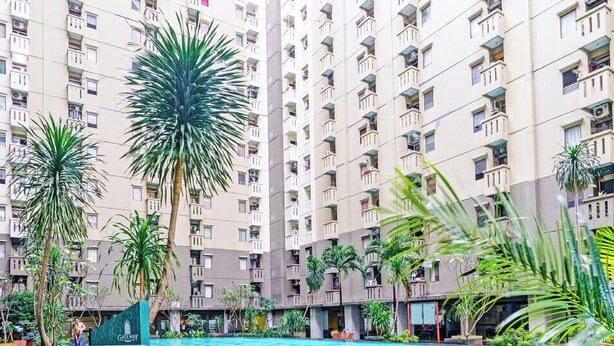 A high-rise residential building with multiple balconies and a central courtyard featuring palm trees and a swimming pool. - OYO Life 92718 Apartement Gateway Cicadas (Bandung)
