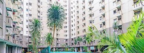 A high-rise residential building with multiple balconies and a central courtyard featuring palm trees and a swimming pool.