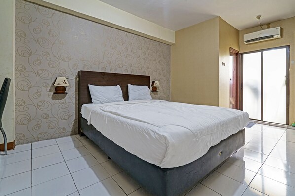 Habitación de hotel con una cama grande, dos mesitas de noche con lámparas, papel tapiz estampado y un ventanal corredizo al exterior.