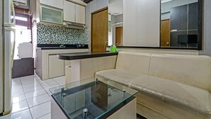 A compact kitchen with a glass coffee table, a sofa, and a tiled backsplash. - OYO Life 92718 Apartement Gateway Cicadas (Bandung)