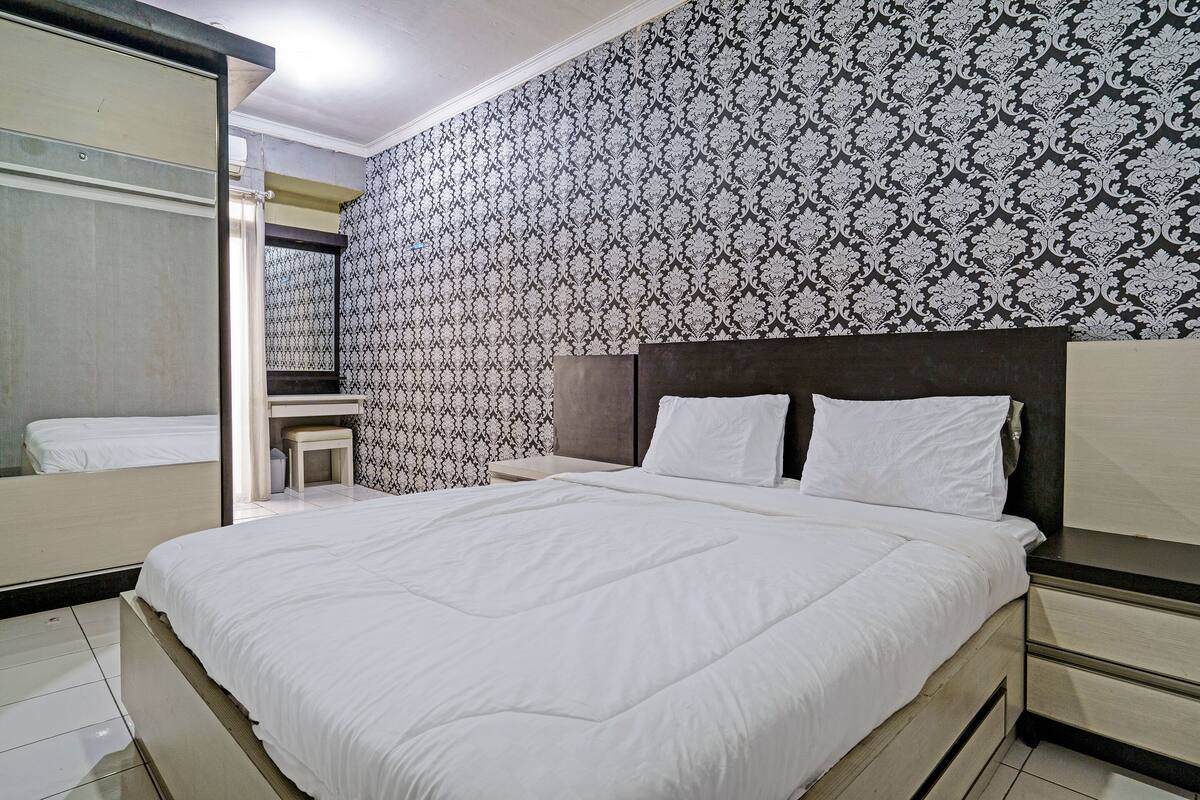 Een hotelkamer met een groot bed, een nachtkastje, een spiegel en behang met een patroon.