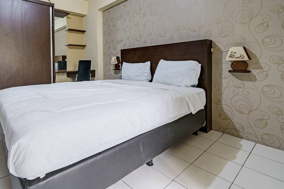 Een net opgemaakt bed met witte lakens in een hotelkamer met behang met een patroon en een houten hoofdeinde.