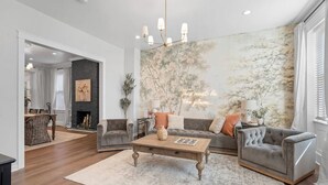 A spacious living room with a fireplace, a large wall mural, and a modern chandelier. - High-End 4bd: hottub, Mini golf, gameroom, firepit (Pittsburgh)