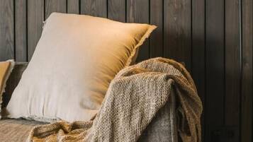 A sofa with a white cushion and a textured blanket draped over it, against a dark wooden wall with a black floor lamp.