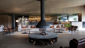 Een moderne lounge met een centraal openhaardelement, banken en een bar op de achtergrond.