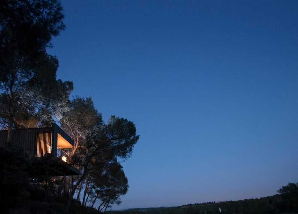Een modern huis met balkon, omringd door bomen, in het schemerlicht.