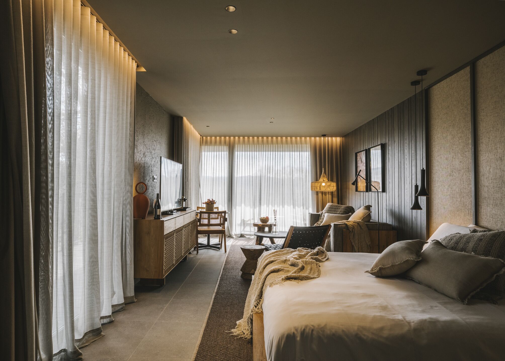 Una habitación de hotel moderna con una cama grande, un escritorio con televisor, una silla y un sofá.