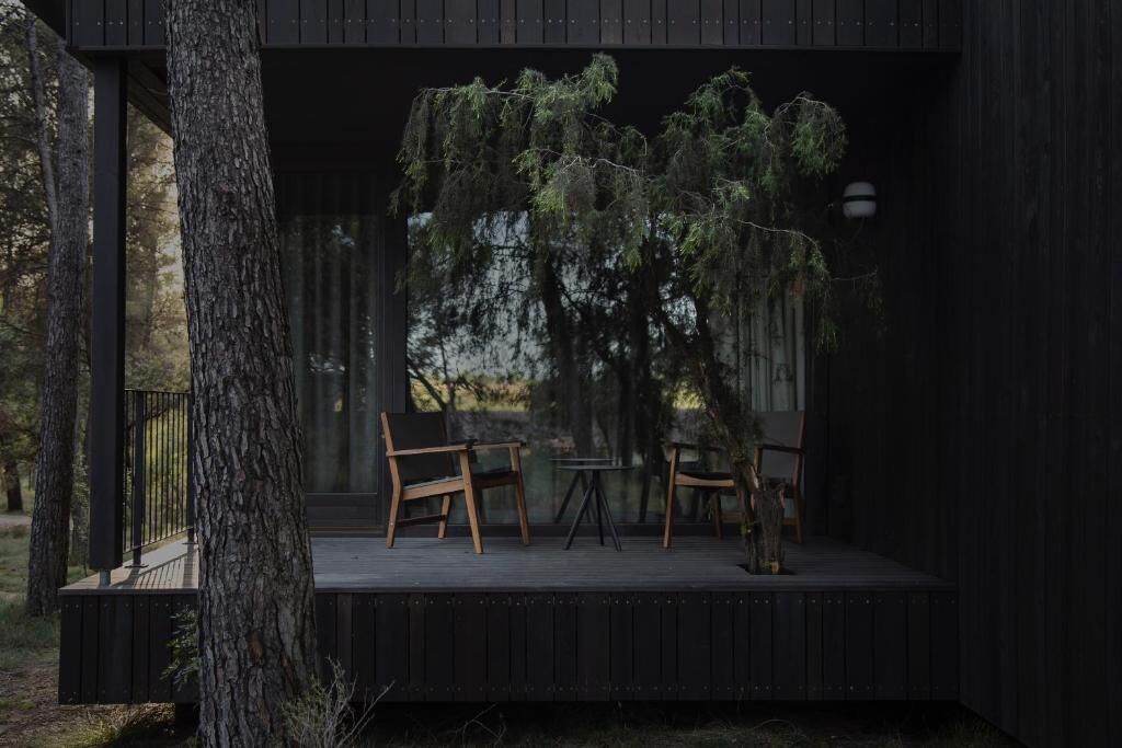 Una terraza de madera con dos sillas y una pequeña mesa, rodeada de árboles.