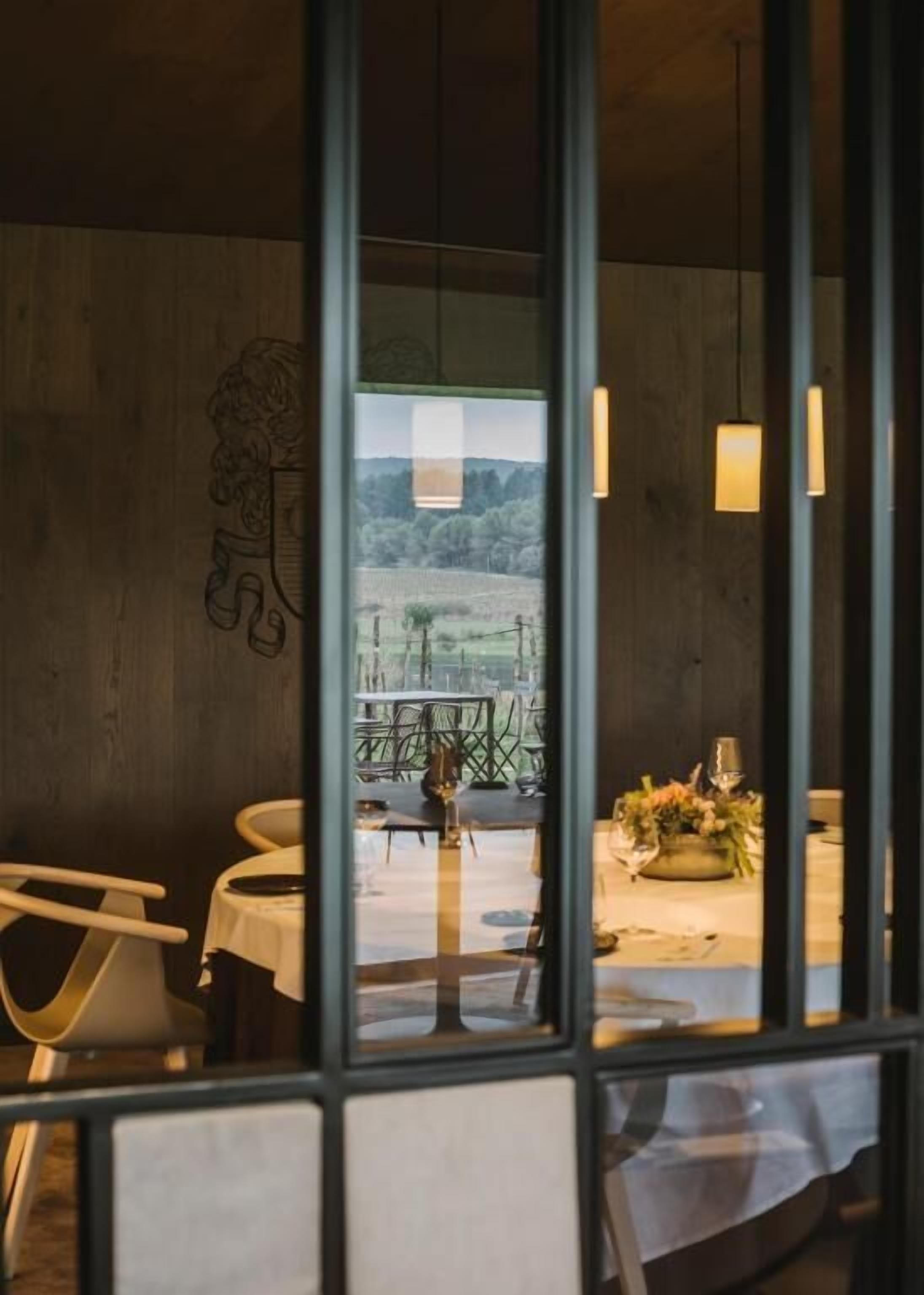 A dining area with a view of a vineyard through a glass partition.
