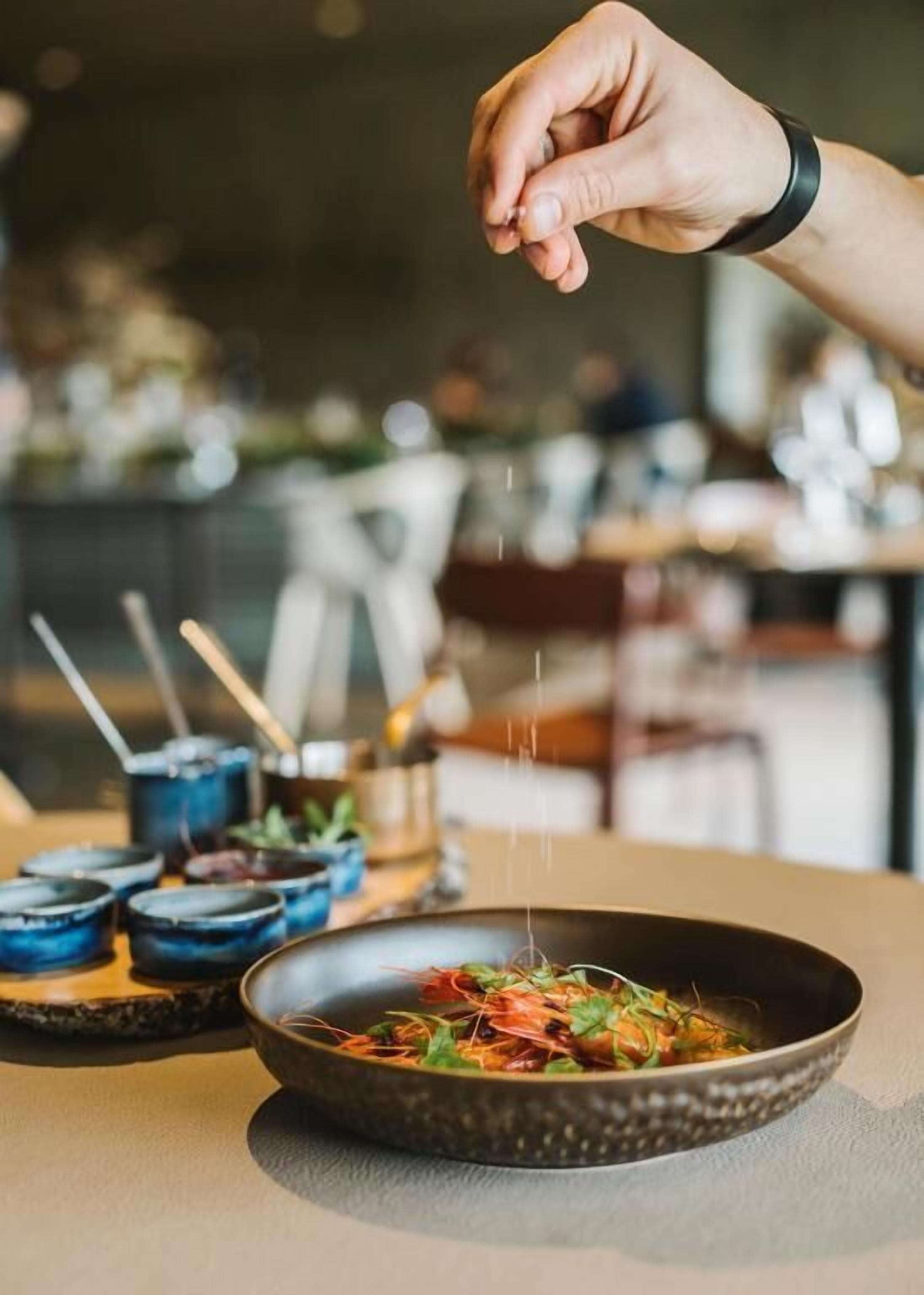 A hand sprinkling seasoning over a dish in a bowl.