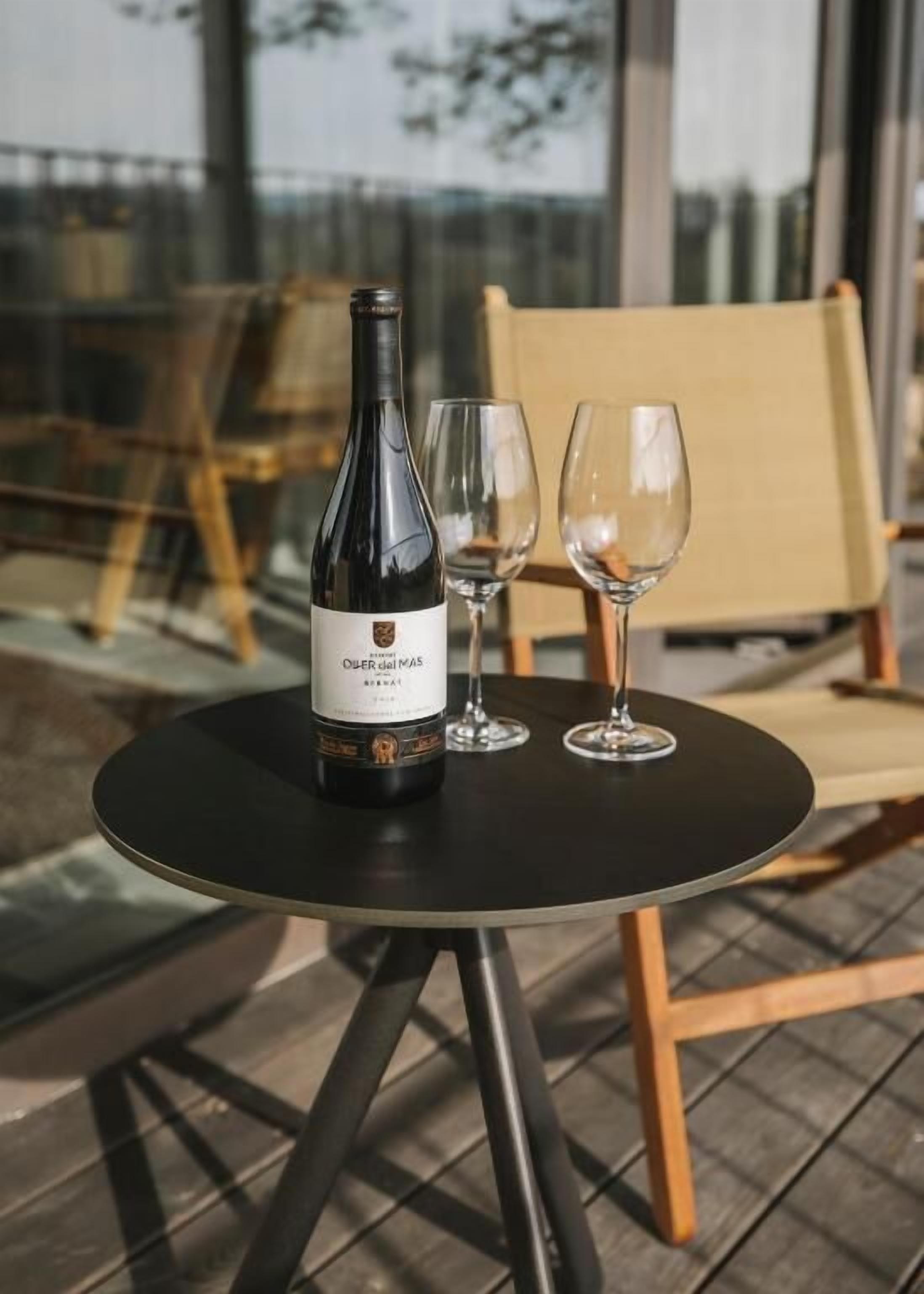 A bottle of wine and two glasses on a round table outdoors.