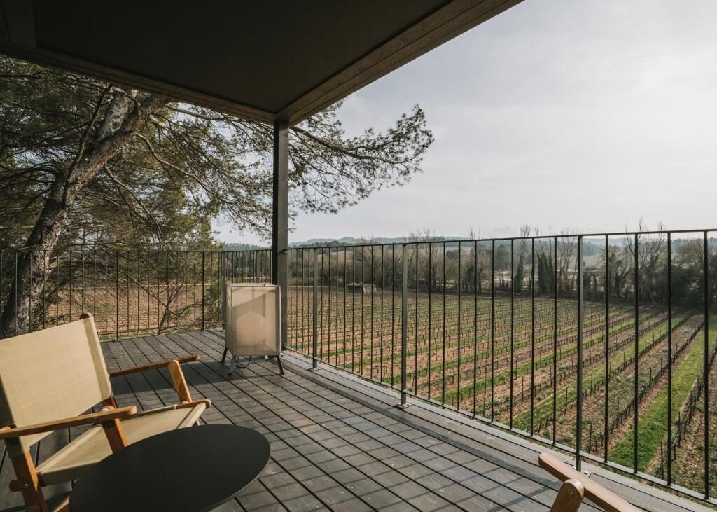 Un balcón con vistas a un viñedo, una silla de madera y una mesa.
