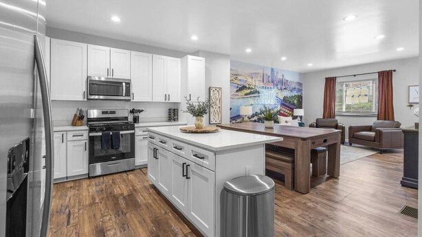 A modern kitchen with white cabinetry, a central island, stainless steel appliances, and a cityscape mural.