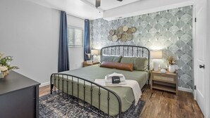 A bedroom with a bed, bedside tables, a ceiling fan, and a patterned wallpaper.