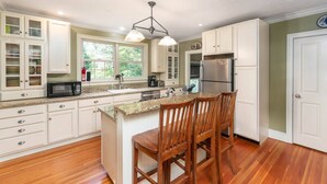 A kitchen with white cabinets, a granite countertop, a stainless steel refrigerator, and a wooden island with bar stools. - Perfect Location in North Conway Village

 (Conway)