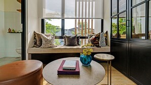 A modern living room with a large window, a sofa with cushions, a small round table with a book and vase, and a brown leather chair. - OYO Life 92719 Rolling Hills Residence Karawang (Karawang)
