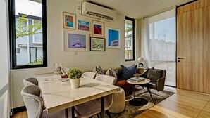 A modern dining area with a marble table, grey upholstered chairs, a small round table with a lamp, and a sofa with cushions. - OYO Life 92719 Rolling Hills Residence Karawang (Karawang)