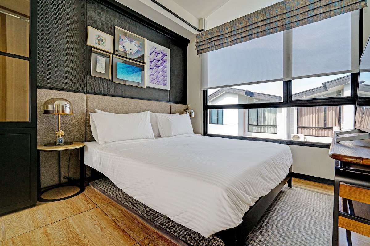 A neatly made bed with white linens, a small bedside table with a lamp, and artwork on the wall.