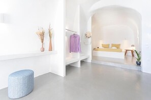 A modern, minimalist hotel room with a white color scheme, a sofa, a bed, and a small table with a lamp. - Eva's Suite with  with Jacuzzi and Sea view. (Fira)