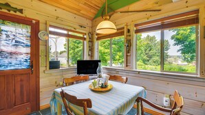 A wooden cabin interior with a dining table set for two, a clock, and a television. - Warm & Cozy Clayton Cabin Near St Lawrence River! (Clayton)