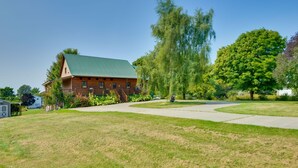 A large log cabin with a green roof, surrounded by a well-maintained lawn and trees. - Warm & Cozy Clayton Cabin Near St Lawrence River! (Clayton)