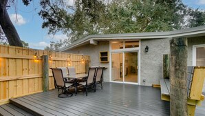 Eine Holzterrasse mit Tisch und Stühlen, ein Holzzaun und ein Gebäude mit einer Schiebetür.