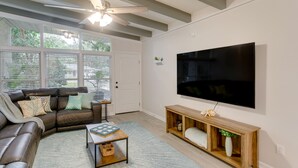 Ein modernes Wohnzimmer mit einem Ecksofa, einem Couchtisch, einem Holzkonsolentisch und einem großen Flachbildfernseher an der Wand.