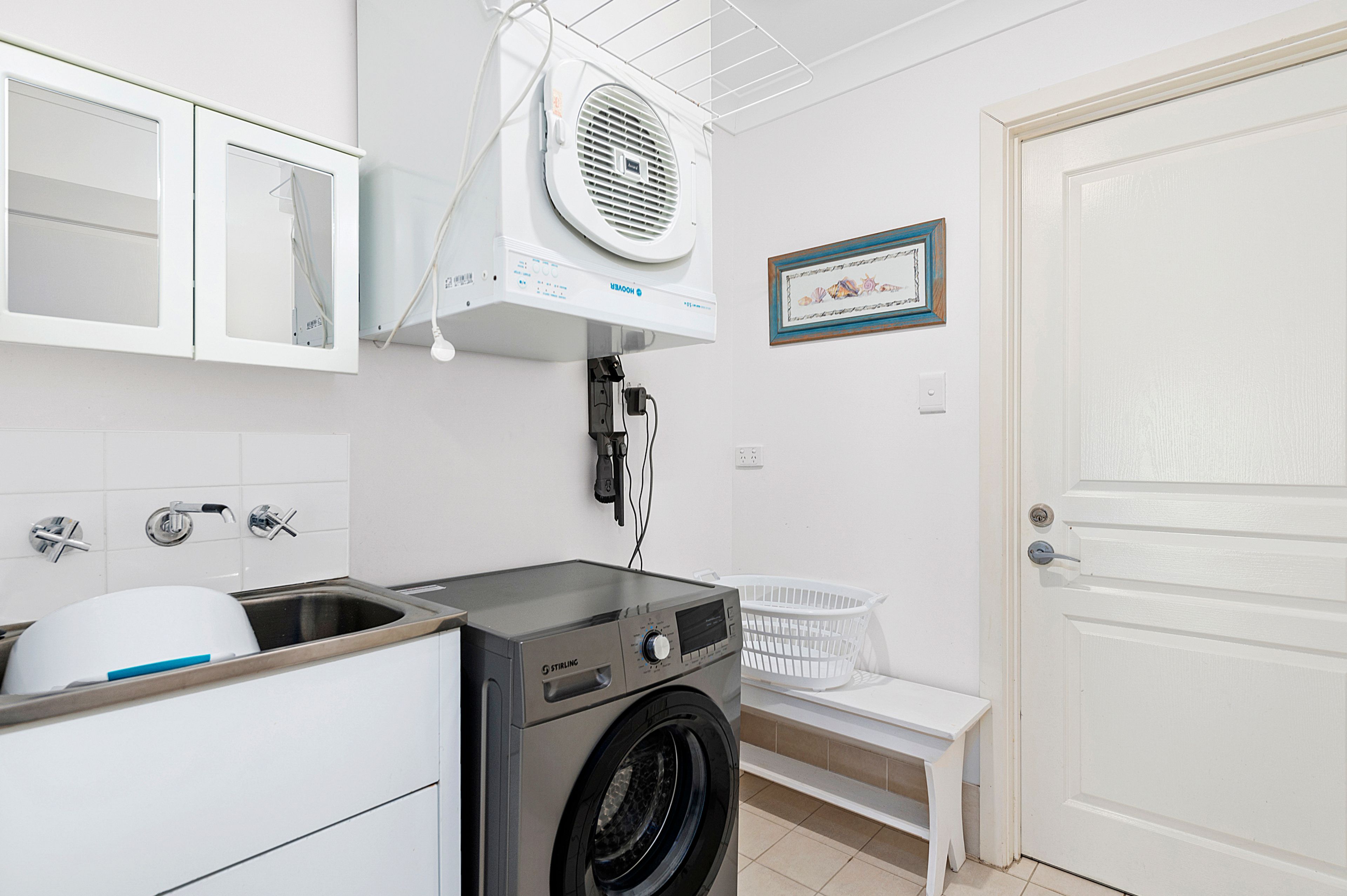 A laundry room with a washing machine, a drying rack, a sink, and a door.
