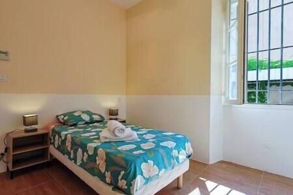 Een slaapkamer met een bed, bedlampen, een nachtkastje en een raam met uitzicht op groen.