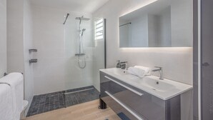 A modern bathroom with a glass-enclosed shower, a large mirror, and two sinks. - Libre Lune (Sainte-Luce)