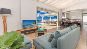 A modern living room with a large TV, a dining area, and a view of the ocean. - Libre Lune (Sainte-Luce)