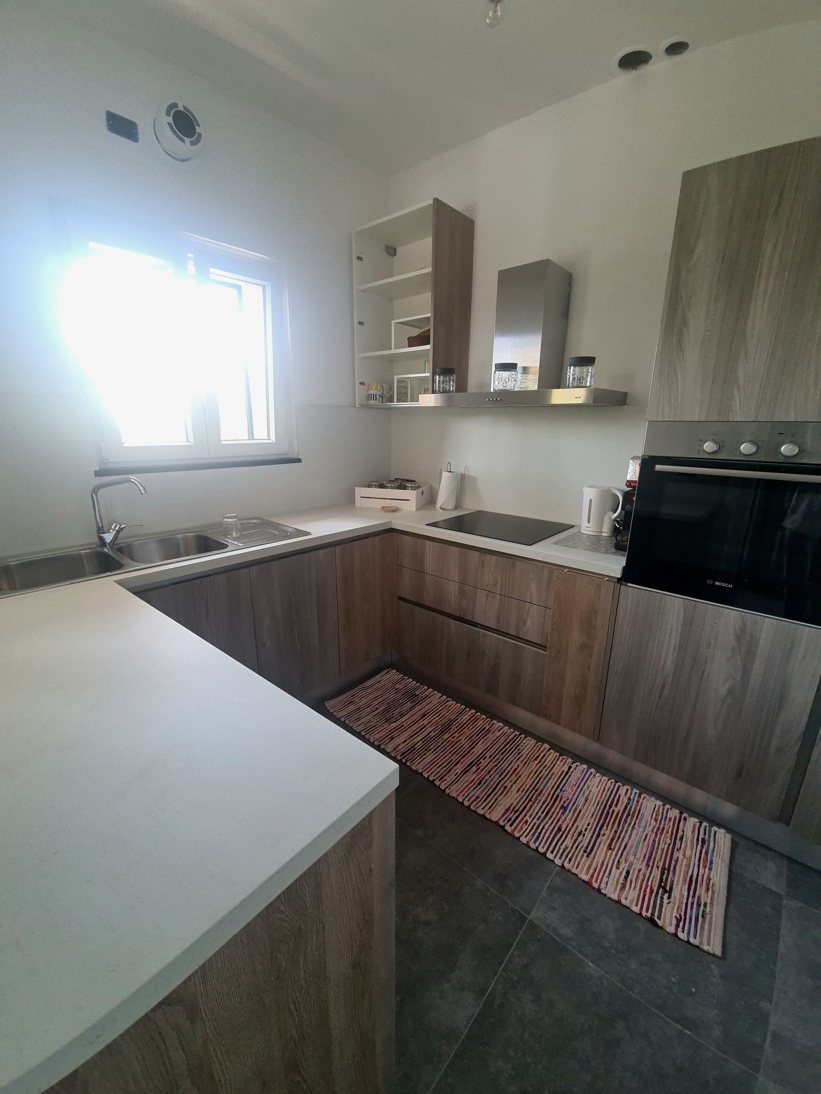 A modern kitchen with wooden cabinets, a built-in oven, and a window providing natural light.