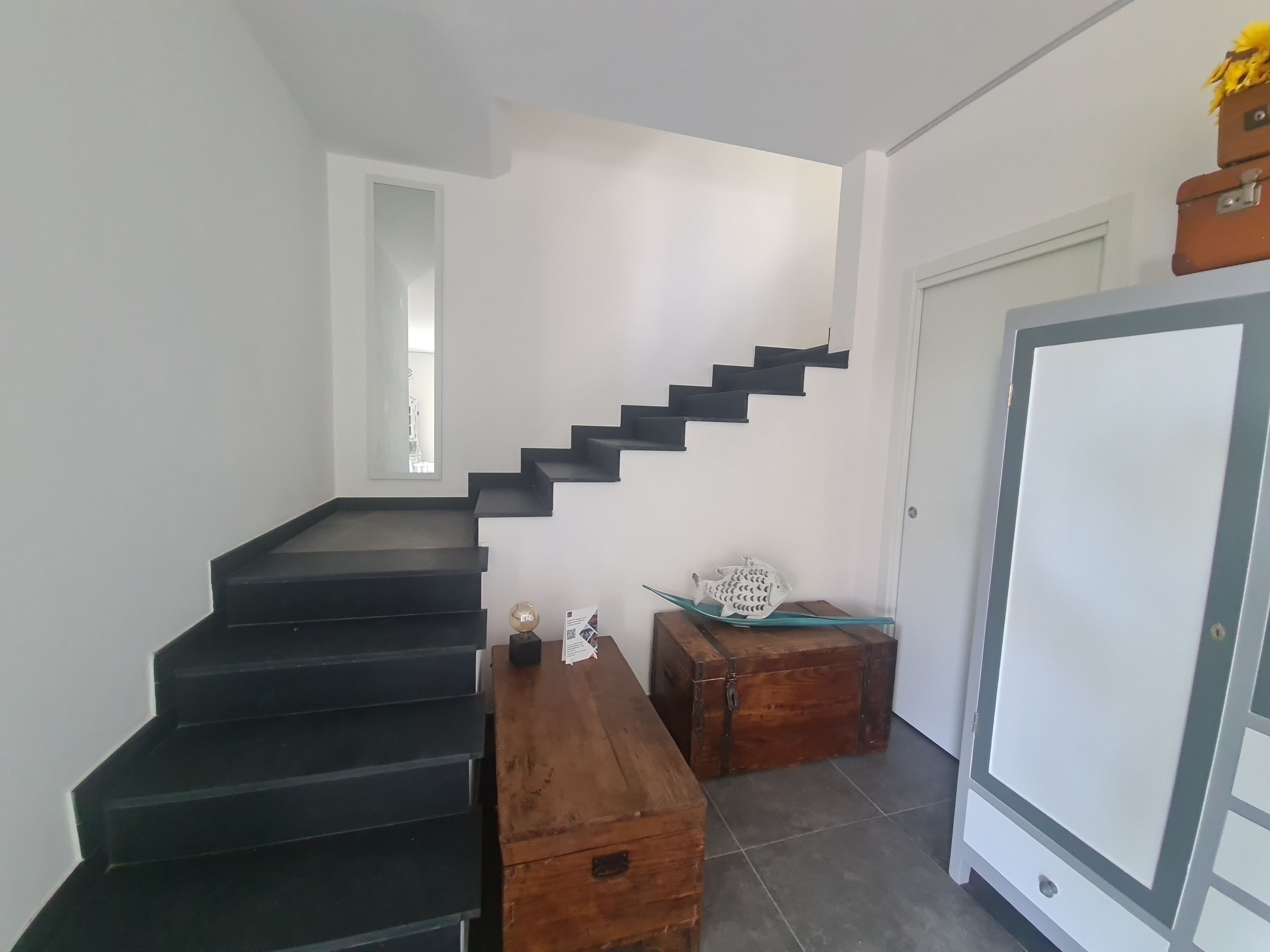 A staircase with black steps leading to a landing. There is a wooden chest and a decorative fish on the landing.